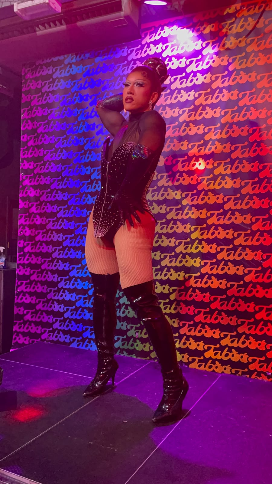 Artista drag no palco, em frente a uma parede com o logótipo do bar Taboo