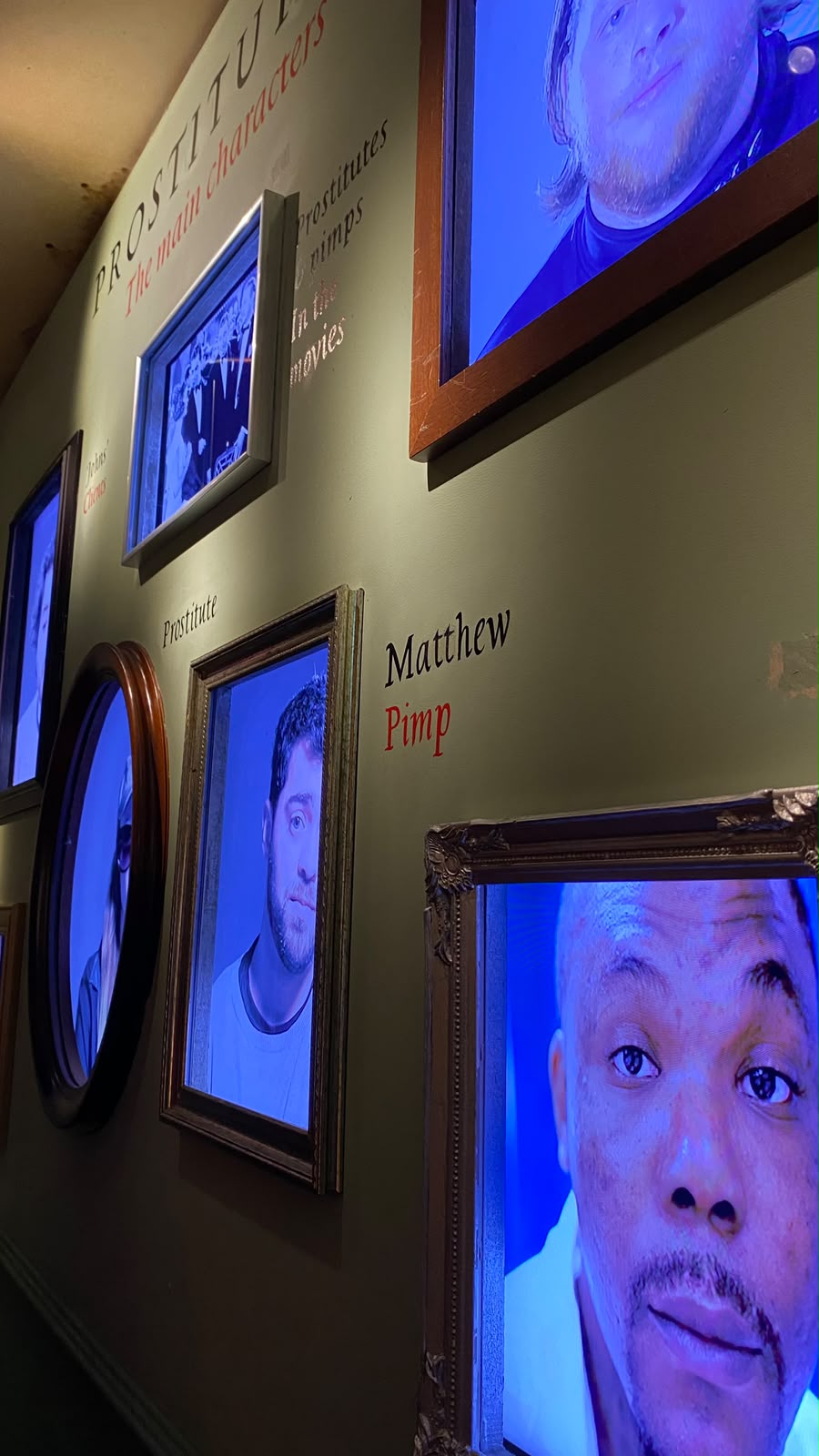 Parede de museu com retratos em vídeo e o título 'Prostitutes: the main characters'