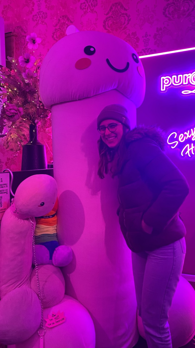 Viajante ao lado de um pénis de peluche gigante cor-de-rosa numa sex shop