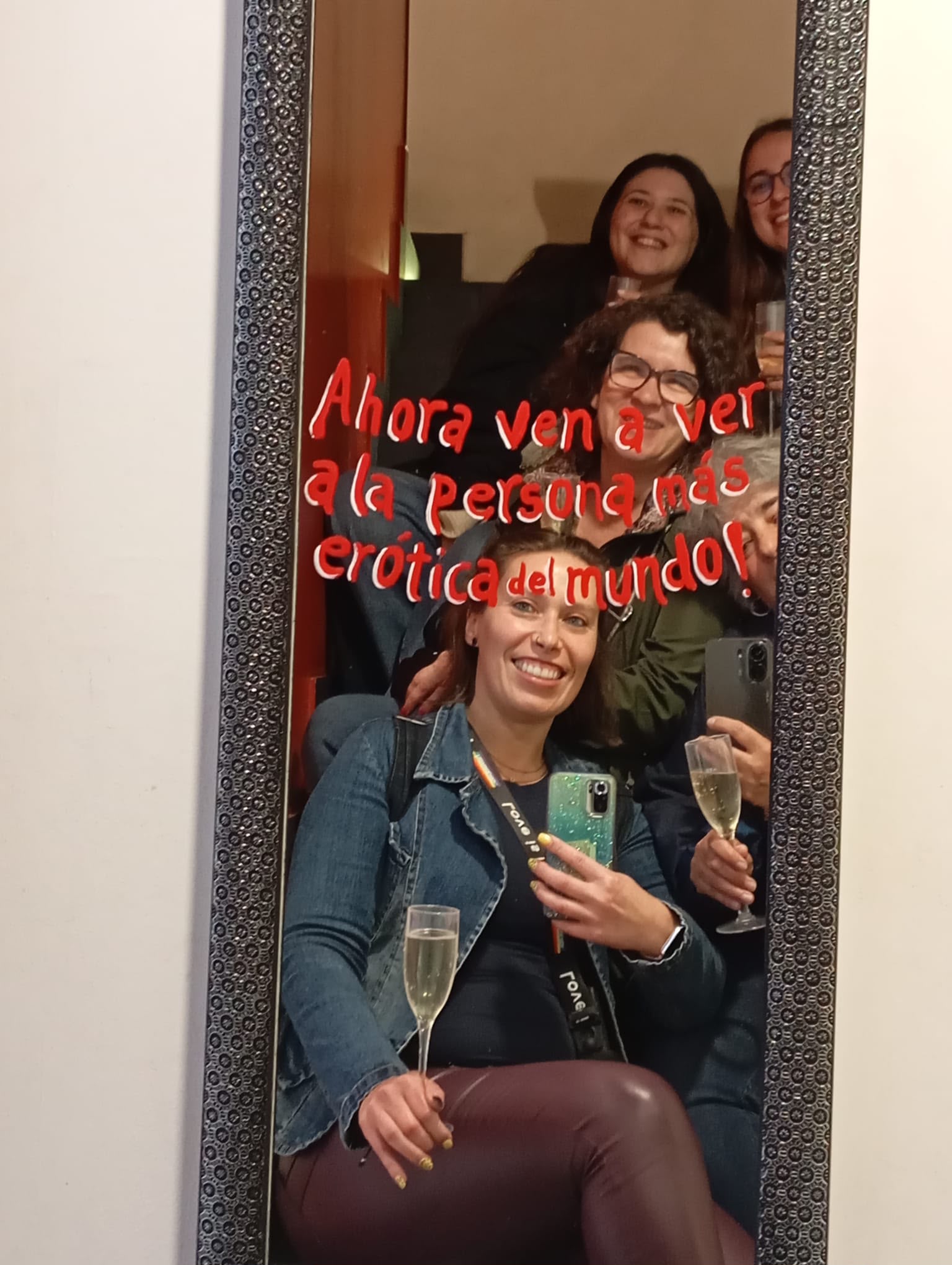Selfie de grupo ao espelho com champanhe e a frase 'Ahora ven a ver a la persona más erótica del mundo'