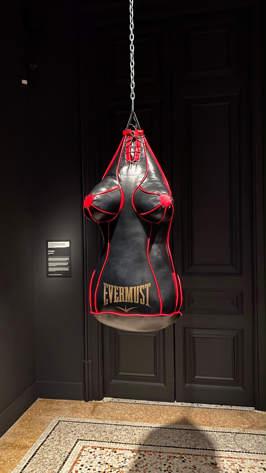 Saco de boxe de couro com a forma de um corpo feminino, pendurado numa galeria escura