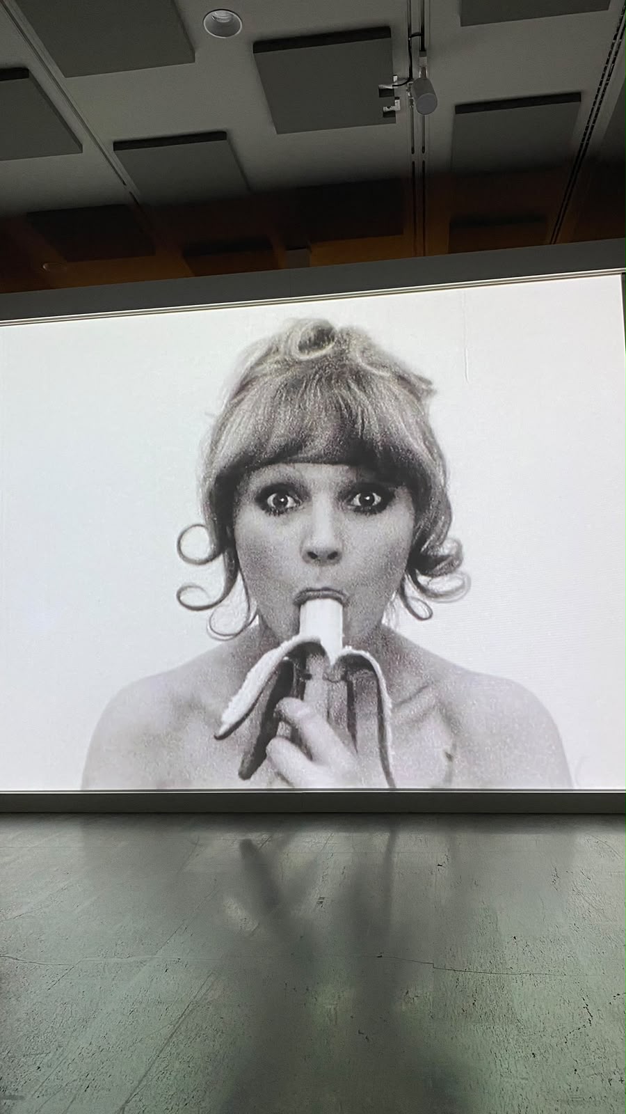 Projeção de vídeo a preto e branco de uma mulher a comer uma banana, numa galeria