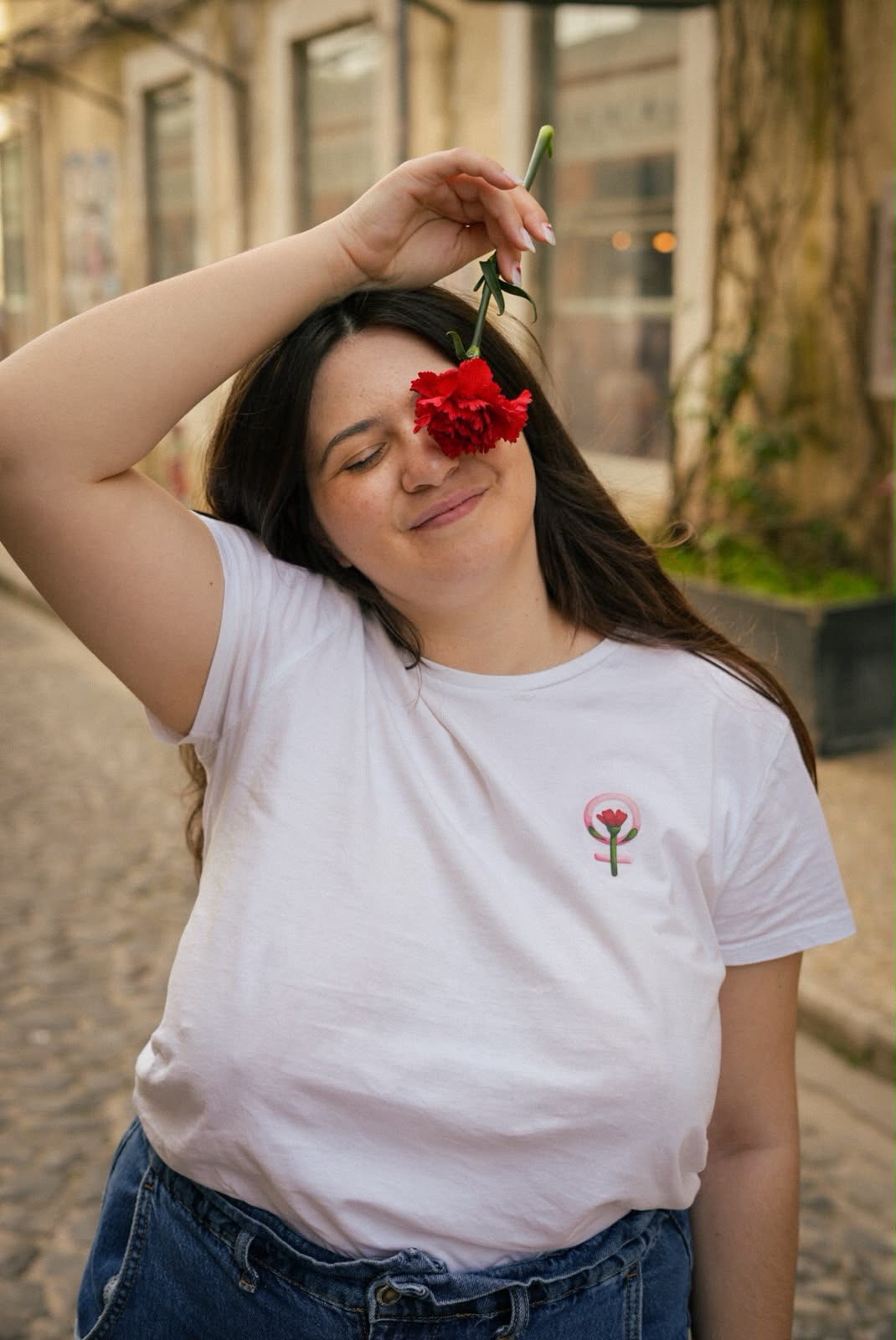 Mulher a segurar um cravo vermelho, com uma t-shirt branca com um símbolo feminista e um cravo