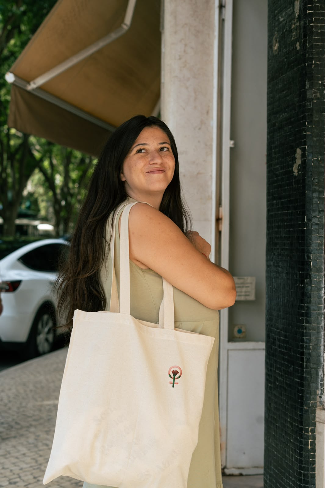 Mulher a sorrir com uma tote bag de lona com um símbolo feminista e um cravo