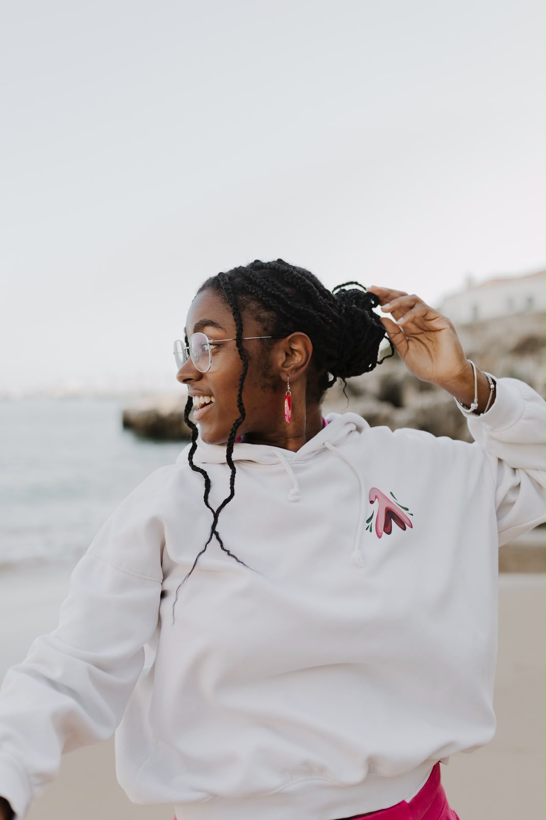 Mulher a rir na praia com uma hoodie branca com a ilustração de um clítoris