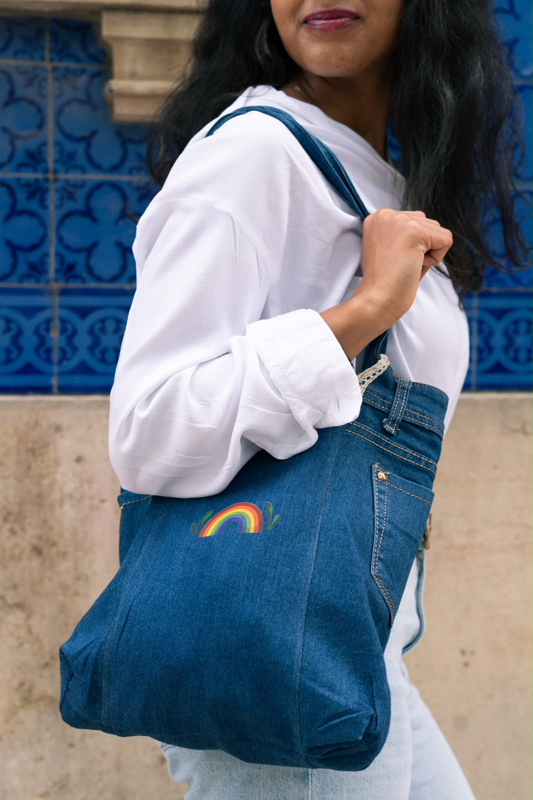 Tote bag de ganga com um pequeno arco-íris, em frente a azulejos portugueses azuis