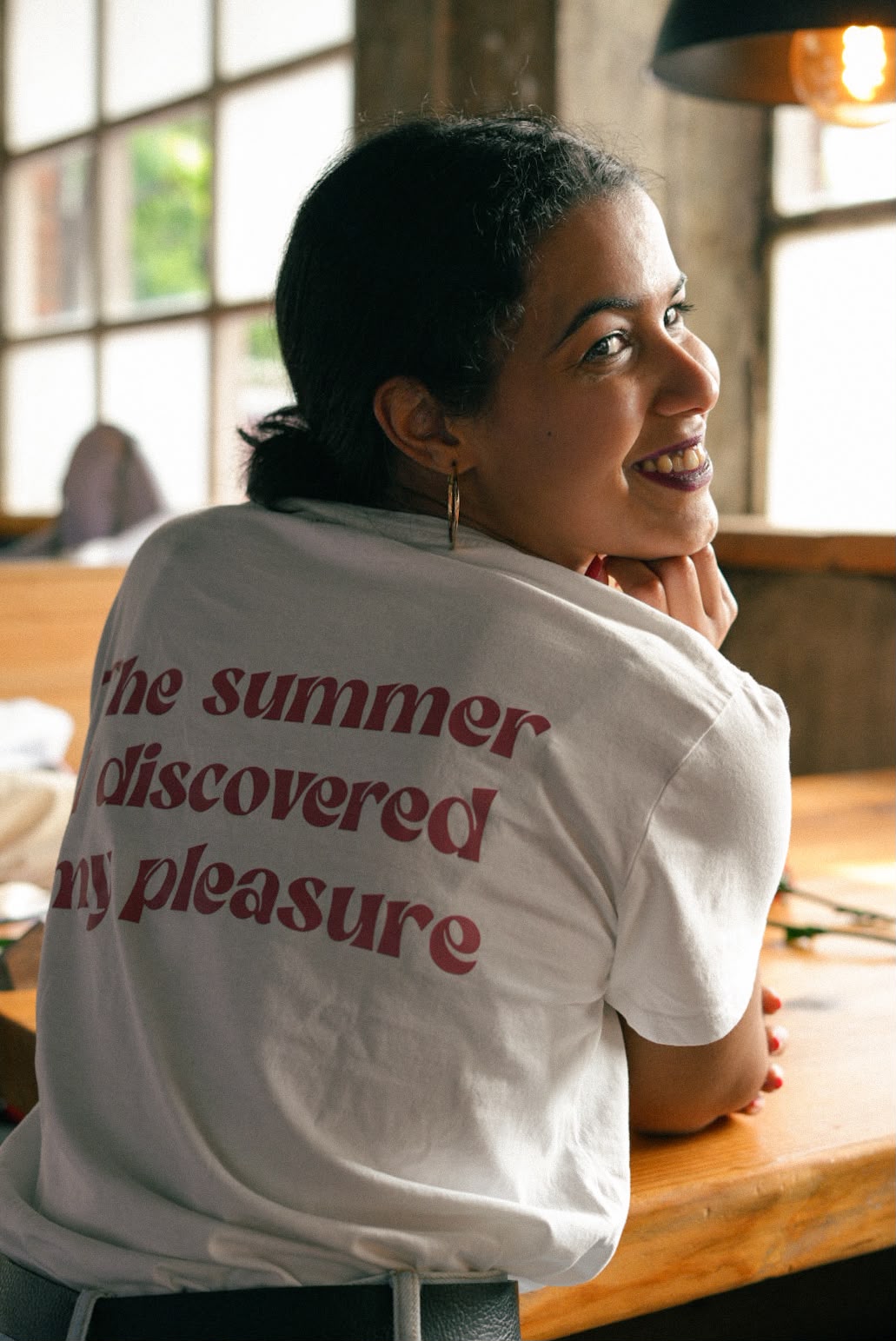 Mulher a sorrir por cima do ombro, com uma t-shirt com a frase 'The summer I discovered my pleasure'