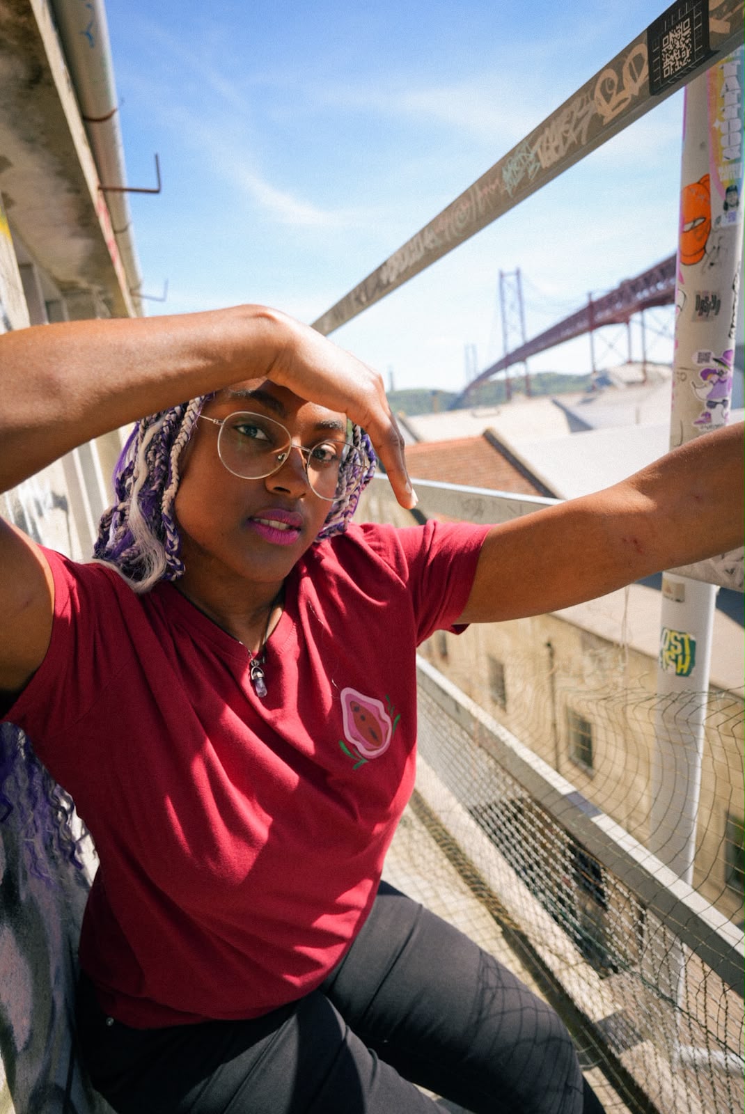 Mulher com uma t-shirt vermelha com a ilustração de uma vulva, com a ponte 25 de Abril atrás