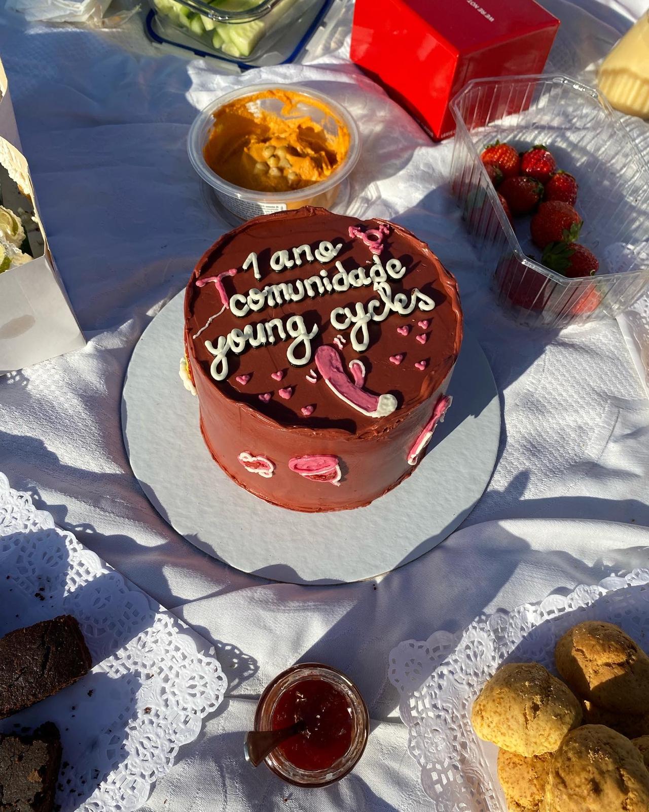 Bolo de chocolate com a frase '1 ano comunidade Young Cycles', num piquenique