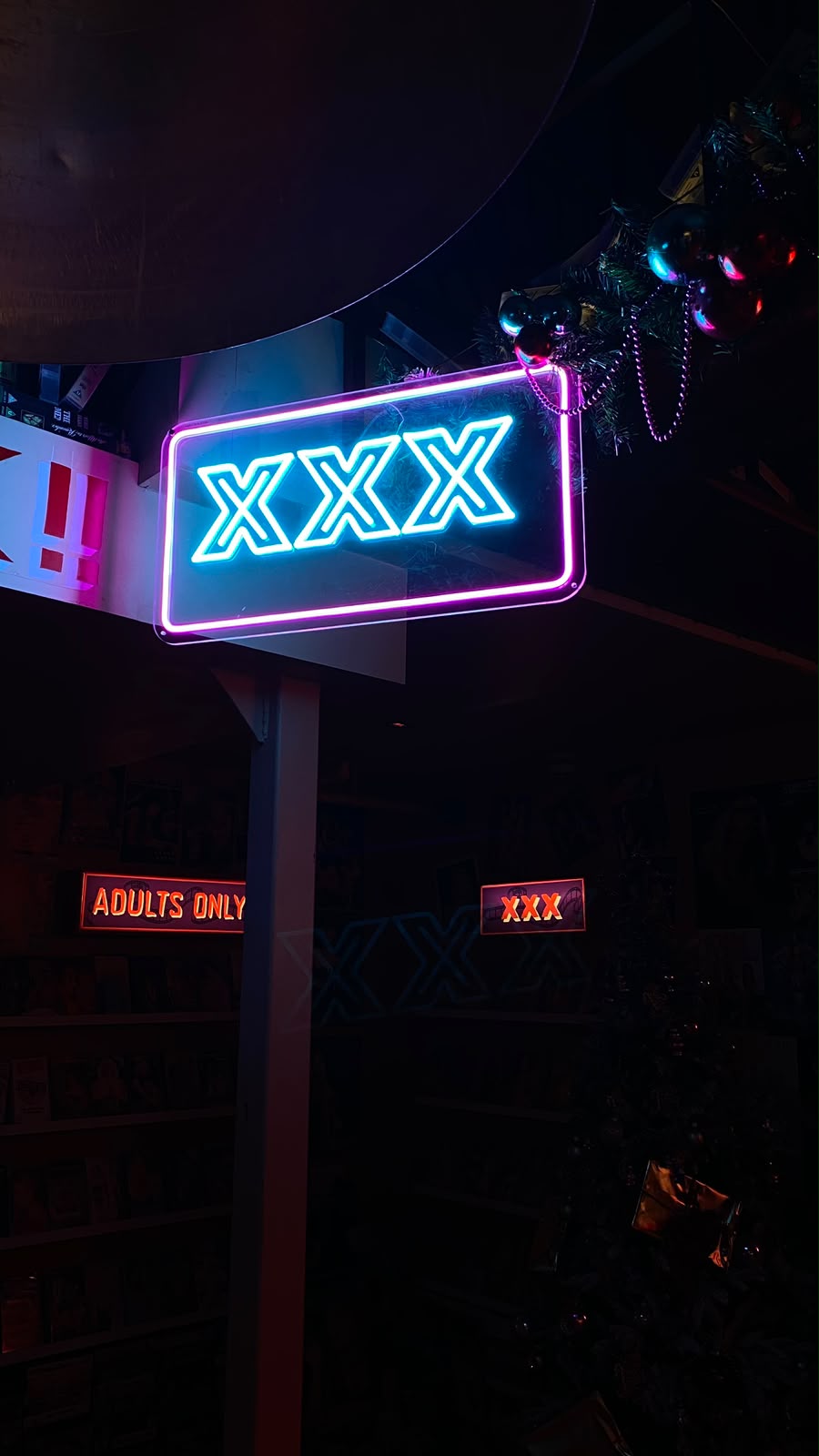 Néon azul e cor-de-rosa com 'XXX' por cima de prateleiras de filmes para adultos