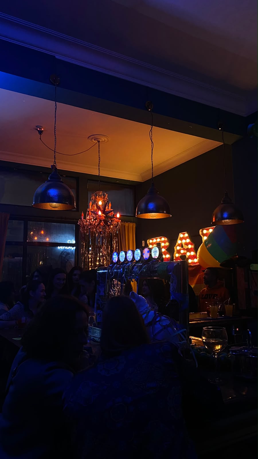 Bar cheio à noite, com letras luminosas e uma bandeira arco-íris