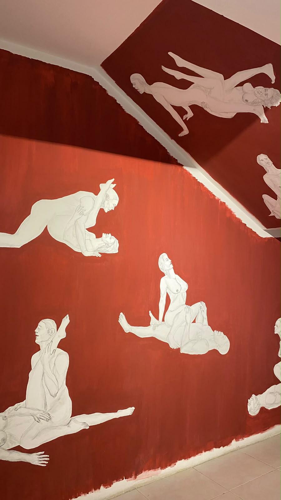 Parede e teto vermelhos pintados com figuras brancas em posições sexuais