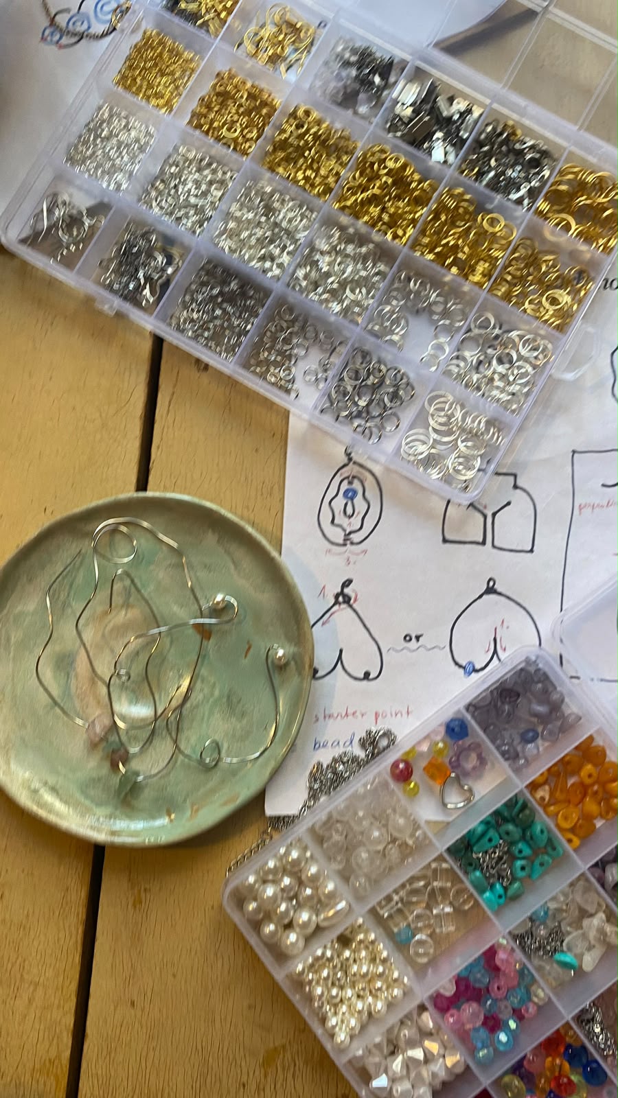 Mesa de um workshop de joalharia com missangas, anéis e desenhos de brincos em forma de vulva