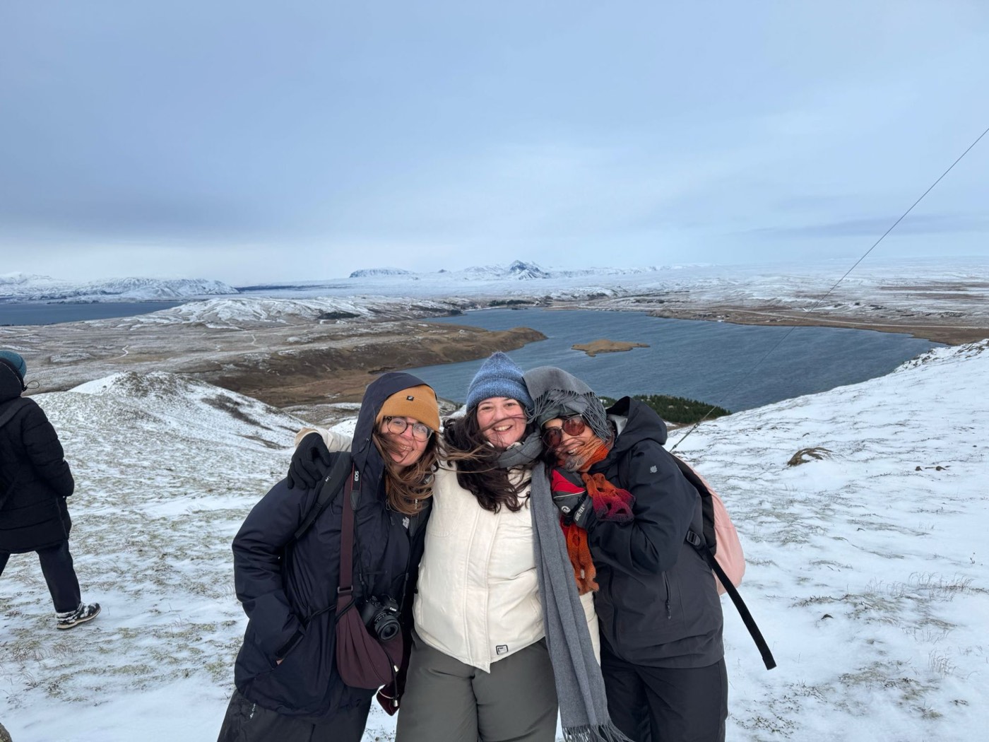 Mariana com duas amigas numa colina com neve, com um lago e montanhas ao fundo, na Islândia