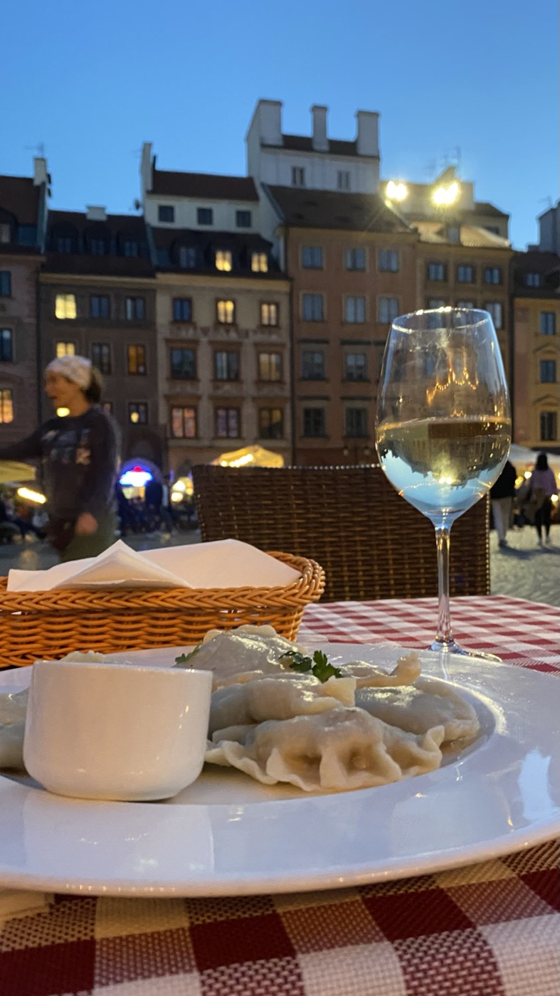 Prato de pierogi e um copo de vinho branco numa esplanada da Praça do Mercado da Cidade Velha de Varsóvia, ao anoitecer